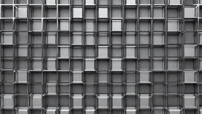 The primary subject of the image is a pattern of square-shaped glass blocks. The setting is a gray background, which contrasts with the glass blocks. The visual style is a close-up of the glass blocks, showcasing their intricate design. The colors and mood of the image are predominantly gray, giving it a modern and minimalist appearance.