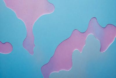 The primary subject of the image is a blue background with pink and purple drips or splatters on it. The setting appears to be a blue surface, possibly a table or a wall. The visual style of the image is a combination of digital art and illustration, as the drips and splatters are created using a digital medium. The colors and mood of the image are predominantly pink and purple, giving it a somewhat moody and artistic atmosphere.
