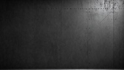 The primary subject of the image is a large, dark grey wall. The setting is a room with a concrete surface, and the visual style is a black and white photo. The dominant colors are grey and black, creating a moody atmosphere.