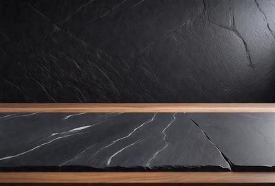 The primary subject of the image is a black marble countertop. The setting is a black wall, which serves as the backdrop for the countertop. The visual style is a photo, capturing the details of the marble countertop and the black wall. The colors and mood of the image are predominantly dark, with the black marble and black wall creating a dramatic and sophisticated atmosphere.