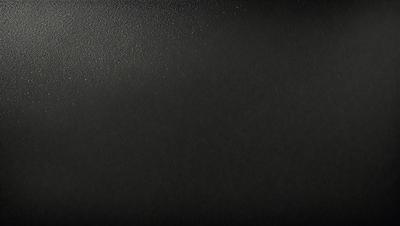 The primary subject of the image is a black background with a leather-like texture. The setting is a dark room, and the visual style is a close-up of the leather-like surface. The colors and mood of the image are predominantly dark and moody, with the black background and leather-like texture creating a dramatic and intense atmosphere.