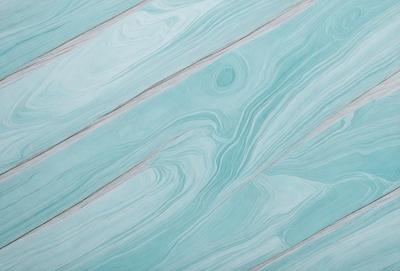 The primary subject of the image is a blue wooden floor with a unique, swirling pattern. The setting is a room with a blue-green color scheme. The visual style is a combination of a photo and a digital art, creating a striking and visually appealing design. The colors and mood of the image are predominantly blue and green, giving it a calm and soothing atmosphere.