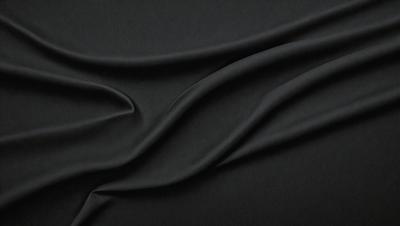The primary subject of the image is a black fabric, which is the main object, scene, or focus of the image. The setting or background is a dark surface, and the visual style appears to be a photo. The colors and mood of the image are predominantly dark and moody, with the black fabric being the dominant color.