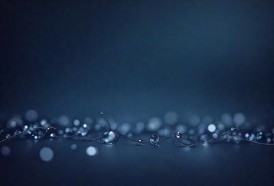 The primary subject of the image is a long, curved line of water droplets, which are floating in the air. The setting is a dark, blue background, which creates a dramatic and moody atmosphere. The visual style is a combination of a photo and digital art, as the droplets are captured in a realistic manner while the overall composition and color palette are artistic. The colors and mood of the image are predominantly dark and mysterious, with the blue background and the floating droplets creating