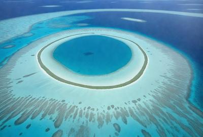 The image features a large, round, blue lagoon with a sandy bottom. The lagoon is surrounded by a coral reef, creating a beautiful and serene underwater scene. The vibrant blue color of the lagoon contrasts with the white sand, making the scene visually appealing. The combination of the lagoon, coral reef, and sandy bottom creates a unique and captivating underwater environment.