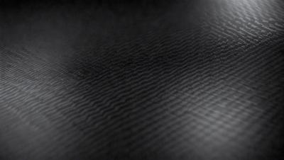 The primary subject of the image is a black leather surface. The setting is a dark room, and the visual style is a close-up of the leather surface. The colors and mood of the image are predominantly dark and moody, with the black leather being the main focus.