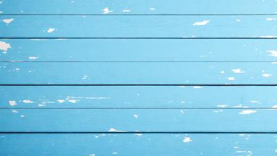 The primary subject of the image is a blue wooden wall with white paint peeling off. The setting is a room with a blue wooden wall, and the visual style is a photo. The dominant colors are blue and white, creating a mood of fading or aged appearance.