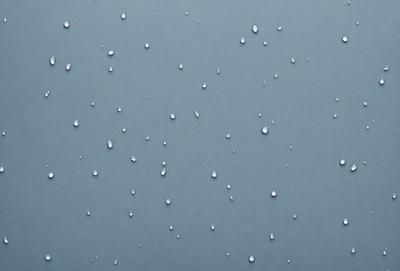 The primary subject of the image is a blue background with a pattern of water droplets. The setting is a gray wall, and the visual style is a close-up of the water droplets. The colors and mood of the image are predominantly blue and calm, with the water droplets creating a soothing and serene atmosphere.