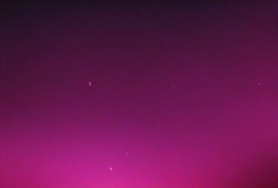 The primary subject of the image is a pink sky with a few stars visible. The setting is a dark, purple background that contrasts with the pink sky. The visual style appears to be a photo, as the image captures the night sky with the stars. The colors and mood of the image are predominantly pink and purple, creating a serene and dreamy atmosphere.