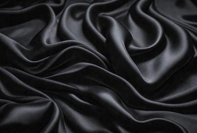 The primary subject of the image is a close-up of a black fabric, possibly a piece of clothing or a curtain. The setting is a black background, which emphasizes the fabric's texture and pattern. The visual style is a close-up, which highlights the fabric's details. The colors and mood of the image are predominantly black, creating a dramatic and moody atmosphere.