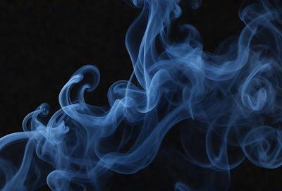 The primary subject of the image is a blue smoke or fog, which is the main object, scene, or focus of the image. The setting or background is a dark, possibly black, surface, which contrasts with the blue smoke. The visual style of the image is a close-up of the smoke, which gives it a more dramatic and intense appearance. The colors and mood of the image are predominantly dark and moody, with the blue smoke serving as the main source of color and visual interest.