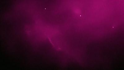 The primary subject of the image is a purple sky with a few stars visible. The setting is a dark, cloudy night with a pinkish hue. The visual style is a combination of a photo and a digital art, creating a unique and artistic representation of the night sky. The colors and mood of the image are predominantly purple and dark, giving it a moody and atmospheric feel.