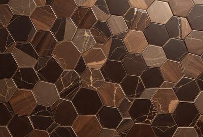 The primary subject of the image is a close-up of a marble tile wall. The setting is a room with a brown and tan color scheme. The visual style is a photo of the tile wall, showcasing its intricate design and texture. The colors and mood of the image are warm and inviting, with the marble tile adding a touch of elegance and sophistication to the space.