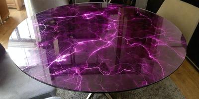 The primary subject of the image is a purple table with a purple marble top. The table is placed on a carpeted floor, and the setting appears to be indoors. The visual style of the image is a photo, and the dominant colors are purple and black. The overall atmosphere of the image is modern and stylish.