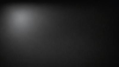 The primary subject of the image is a black background with a white light source. The setting is a dark room, and the visual style is a black and white photo. The colors and mood of the image are predominantly dark and moody, with the white light source creating a stark contrast against the black background.