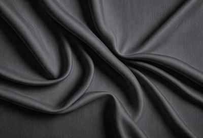The primary subject of the image is a close-up of a piece of fabric, likely a piece of clothing or a curtain. The setting is a dark background, which emphasizes the fabric's texture and pattern. The visual style appears to be a photo, as it captures the details of the fabric. The colors and mood of the image are predominantly dark, with the fabric being the main focus.