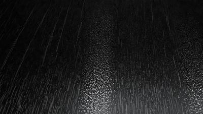 The primary subject of the image is a rainy street with a wet road. The setting is a black background, which adds to the overall mood of the scene. The visual style is a combination of a photo and a drawing, creating a unique and artistic representation of the rainy street. The colors are predominantly black and white, with some grays and shades of blue, giving the image a moody and atmospheric feel.