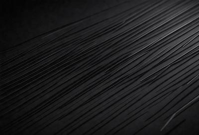 The primary subject of the image is a close-up of a black background with a pattern of thin, white lines. The setting appears to be a dark room, and the visual style is a black and white photo. The dominant colors are black and white, creating a moody and dramatic atmosphere.
