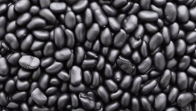The primary subject of the image is a close-up of a large pile of black beans. The beans are arranged in a dense, tightly packed manner, creating a visually striking pattern. The setting is a black background, which emphasizes the beans and their texture. The visual style is a close-up, which allows the viewer to appreciate the details of the beans. The colors and mood of the image are predominantly black, giving it a bold and striking appearance.