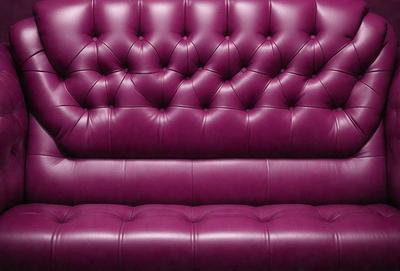 The primary subject of the image is a purple leather couch. The setting is a room with a purple couch as the main focus. The visual style is a photo, and the dominant colors are purple and pink. The overall atmosphere is cozy and inviting.