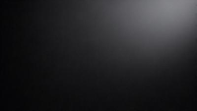 The primary subject of the image is a black background with a white light source. The setting is a dark room, and the visual style is a black and white photo. The colors and mood of the image are predominantly dark and moody, with the white light source providing a contrasting element.