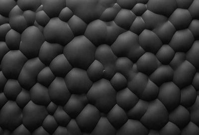 The primary subject of the image is a black and white patterned surface, which appears to be a black leather or fabric material. The setting is a close-up of the pattern, showcasing the intricate design and texture. The visual style is a combination of a photo and a digital art or illustration, as the pattern is both detailed and visually appealing. The colors and mood of the image are predominantly black and white, creating a sense of depth and contrast.