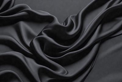 The primary subject of the image is a black fabric, which is the main object, scene, or focus of the image. The setting or background is a dark surface, which provides a contrasting backdrop for the fabric. The visual style of the image is a close-up of the fabric, showcasing its texture and details. The colors and mood of the image are predominantly dark, with the black fabric being the dominant color, creating a moody and dramatic atmosphere.