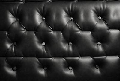 The primary subject of the image is a black leather couch with a patterned design. The couch is the main object in the scene, and it is set against a black background. The visual style of the image is a close-up of the couch, showcasing its unique pattern. The colors and mood of the image are predominantly black, giving it a sleek and modern appearance.