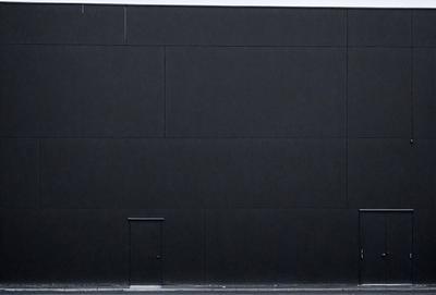 The primary subject of the image is a black wall with a door. The setting is a black building, and the visual style appears to be a photo. The dominant colors are black and white, creating a stark and minimalist atmosphere.