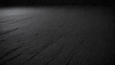The primary subject of the image is a black surface, which appears to be a piece of leather or a similar material. The setting is a dark room, and the visual style is a close-up of the black surface. The colors and mood of the image are predominantly dark and moody, with the black surface being the main focus.