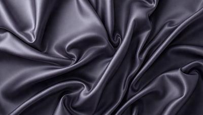 The primary subject of the image is a close-up of a black fabric, possibly a piece of silk or velvet. The setting is a dark background, which emphasizes the fabric's texture and color. The visual style appears to be a close-up or macro shot of the fabric, showcasing its intricate details. The colors and mood of the image are predominantly dark, with the black fabric serving as the focal point.