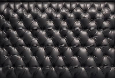 The primary subject of the image is a black leather couch with a patterned design. The couch is set against a black background, giving it a bold and striking appearance. The visual style of the image is a close-up of the couch, showcasing its unique pattern and texture. The colors and mood of the image are predominantly black, creating a sleek and modern atmosphere.