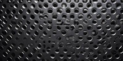 The primary subject of the image is a close-up of a black surface with a pattern of small holes. The setting is a black background, and the visual style appears to be a pattern or texture. The dominant colors are black and grey, creating a somewhat dark and moody atmosphere.