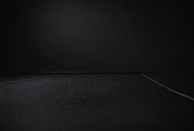 The primary subject of the image is a black background with a white dot. The setting is a dark room, and the visual style is a black and white photo. The colors and mood of the image are predominantly dark and moody, with the white dot being the only bright spot in the scene.