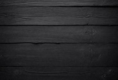 The primary subject of the image is a wooden wall with a black surface. The setting is a room with a black wall, and the visual style is a black and white photo. The colors and mood of the image are predominantly dark and moody, creating a dramatic atmosphere.