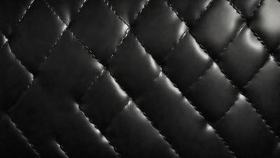 The primary subject of the image is a close-up of a black leather jacket with a quilted pattern. The setting is a black background, which emphasizes the leather jacket's texture and design. The visual style is a close-up, focusing on the details of the jacket. The colors and mood of the image are predominantly black, giving it a sleek and modern appearance.