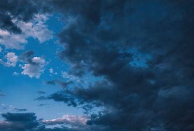 The primary subject of the image is a cloudy blue sky with dark clouds. The setting is a cloudy day, and the visual style is a photo. The dominant colors are blue and dark, creating a moody atmosphere.