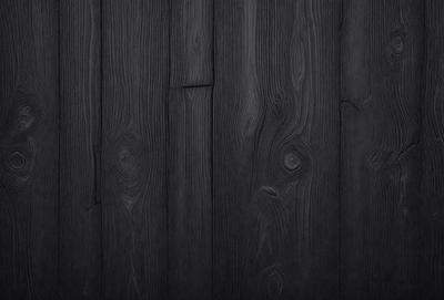 The primary subject of the image is a wooden floor with a black background. The setting is a room with a wooden floor, and the visual style is a close-up of the wooden floor. The colors and mood of the image are dark and moody, with the black wooden floor being the dominant color.
