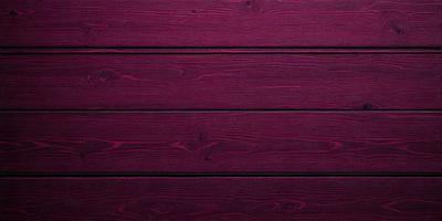 The primary subject of the image is a wooden wall with a purple tint. The setting is a room with a wooden surface, and the visual style is a close-up of the wooden wall. The dominant colors are purple and brown, creating a warm and cozy atmosphere.