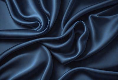 The primary subject of the image is a blue fabric, which appears to be a piece of silk. The setting is a close-up view of the fabric, showcasing its texture and intricate patterns. The visual style is a detailed, up-close representation of the fabric, emphasizing its texture and color. The colors and mood of the image are predominantly blue, creating a calm and serene atmosphere.