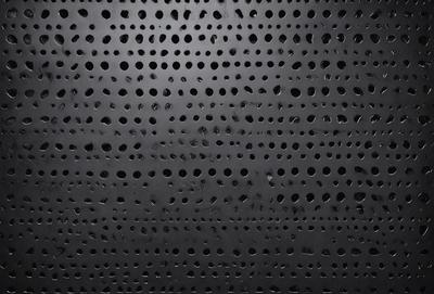 The primary subject of the image is a black background with a pattern of small holes. The setting is a dark room, and the visual style appears to be a close-up of the pattern. The dominant colors are black and white, and the overall atmosphere is somewhat mysterious and intriguing.