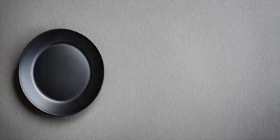 The primary subject of the image is a black plate. The plate is mounted on a wall, and it appears to be a decorative piece. The setting is a white wall, which serves as the background for the plate. The visual style of the image is a close-up of the plate, showcasing its design and texture. The colors and mood of the image are predominantly black and white, giving it a classic and elegant appearance.