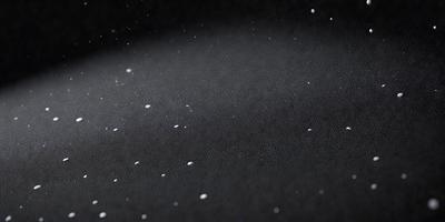 The primary subject of the image is a black background with white specks or dots scattered across it. The setting appears to be a dark room, and the visual style is a close-up of the black background with the white specks. The colors and mood of the image are predominantly dark and moody, with the white specks adding a touch of contrast and interest to the overall composition.