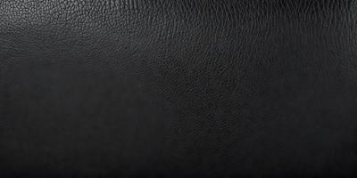 The primary subject of the image is a black leather material. The setting is a black background, which creates a contrast with the leather material. The visual style is a close-up of the leather material, showcasing its texture and details. The colors and mood of the image are predominantly dark, with the black leather material being the main focus.