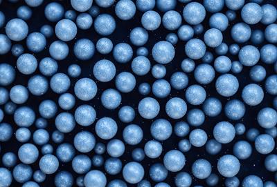 The primary subject of the image is a large number of blue spheres, which are arranged in a pattern. The setting is a dark background, which contrasts with the bright blue spheres. The visual style is a close-up of the spheres, showcasing their unique shapes and textures. The colors and mood of the image are predominantly blue, creating a calm and serene atmosphere.