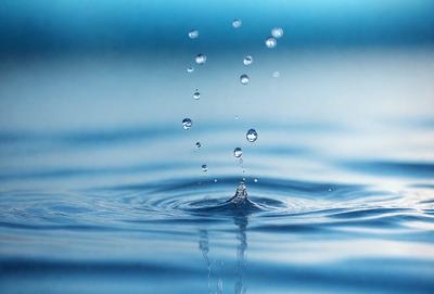The primary subject of the image is a splash of water, which is captured in a close-up shot. The water appears to be falling from a height, creating a dynamic and visually interesting scene. The setting is a blue surface, which could be a pool, a lake, or a waterfall. The visual style of the image is a close-up, which emphasizes the details of the water splash. The colors in the image are predominantly blue, which adds to the overall mood of the scene.