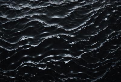 The primary subject of the image is a black and white photo of a body of water, possibly an ocean or a lake. The setting is a dark, black background, which contrasts with the water. The visual style is a black and white photo, giving it a classic and timeless appearance. The colors and mood of the image are predominantly dark, with the water being the main focus and the background serving as a stark contrast.