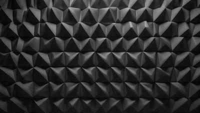 The primary subject of the image is a black wall with a pattern of geometric shapes, resembling a diamond or hexagonal design. The setting is a dark room, and the visual style appears to be a close-up of the wall. The dominant colors are black and grey, creating a moody atmosphere.