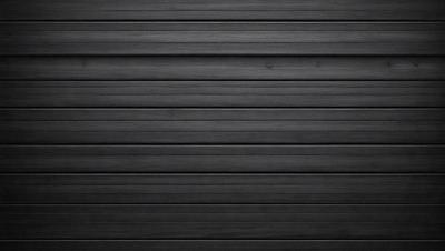 The primary subject of the image is a black wall with a row of black panels. The setting is a dark room, and the visual style is a black and white photo. The dominant colors are black, and the overall atmosphere is moody and dramatic.