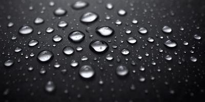 The primary subject of the image is a close-up of a black surface with numerous droplets of water on it. The setting is a dark background, and the visual style appears to be a photo. The colors and mood of the image are predominantly dark, with the droplets of water being the main focus.